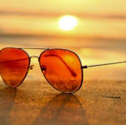Sunglasses in the sand at a beach set against the sun setting