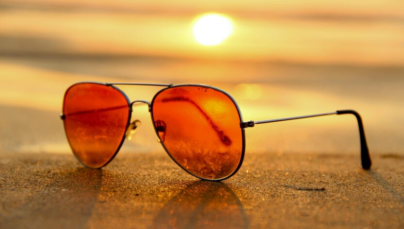 Sunglasses in the sand at a beach set against the sun setting