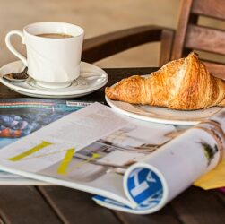 Table at a cafe with two print magazines and a cup of coffee and a croissant.